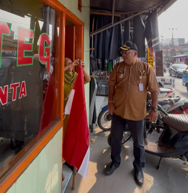Lurah Beji, Samsu Sadikin turun tangan membagikan bendera Merah Putih kepada pelaku usaha yang belum memiliki bendera untuk dipasang di tempatnya masing-masing, Kamis (13/08/26). (Sumber foto: Dokumentasi narasumber)