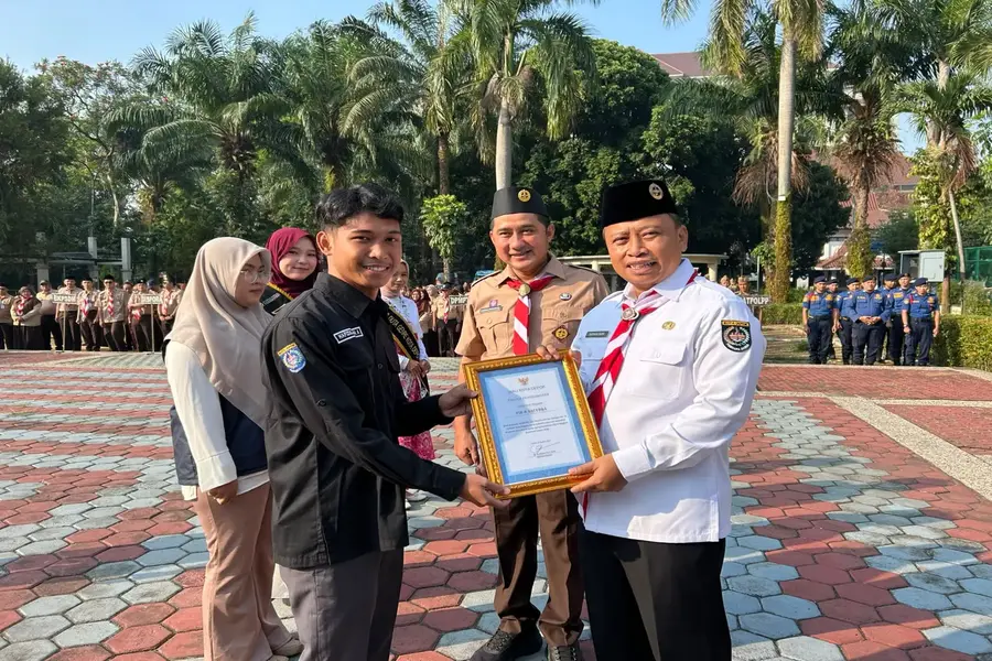 Wali Kota Depok, Supian Suri, menyerahkan penghargaan kepada Ketua PIK-R Sacerba, Hafizul Idham, yang sukses meraih posisi tiga besar di tingkat nasional. Penyerahan dilakukan dalam agenda Apel Pagi di Halaman Balai Kota Depok pada Senin (14/9/2026). (Foto: Diskominfo Depok)