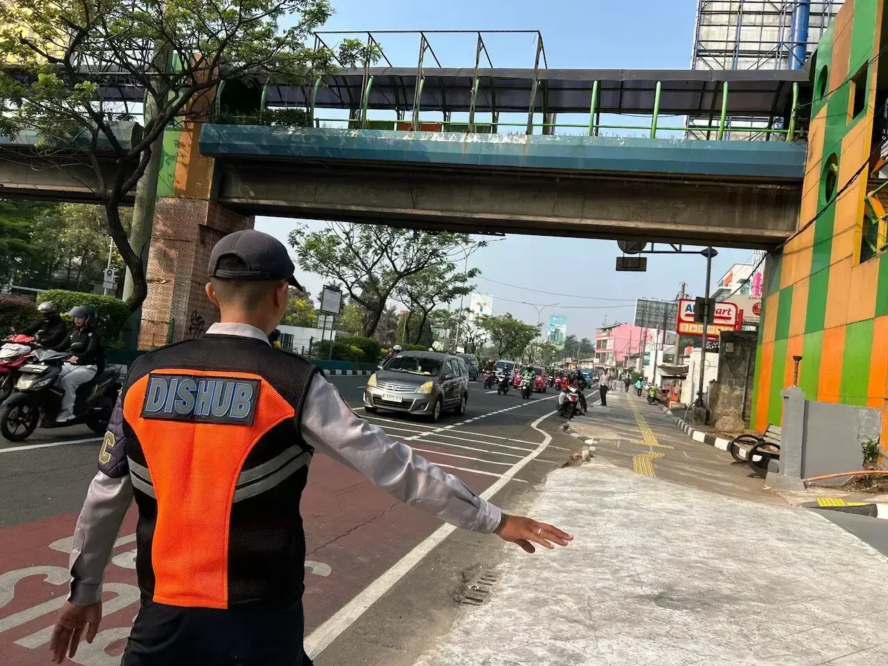 Petugas Dinas Perhubungan (Dishub) Kota Depok mengarahkan kendaraan yang akan masuk ke area Balai Kota Depok untuk melewati akses baru di dekat Jembatan Penyeberangan Orang (JPO) pada Rabu (07/10/26) pagi. (Sumber foto: Diskominfo Depok)