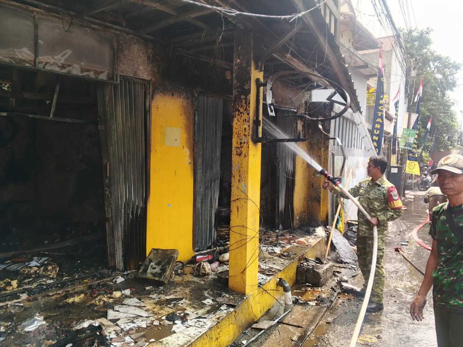 Anggota Koramil 02/Beji mendampingi petugas Dinas Pemadam Kebakaran dan Penyelamatan Kota Depok dalam memadamkan api yang membakar sebuah kios di Jalan H.M. Thohir, RT 01 RW 02 No. 12, Kelurahan Pondok Cina, Kecamatan Beji, pada Rabu (21/10/26). (Foto: Dokumentasi Koramil Beji)