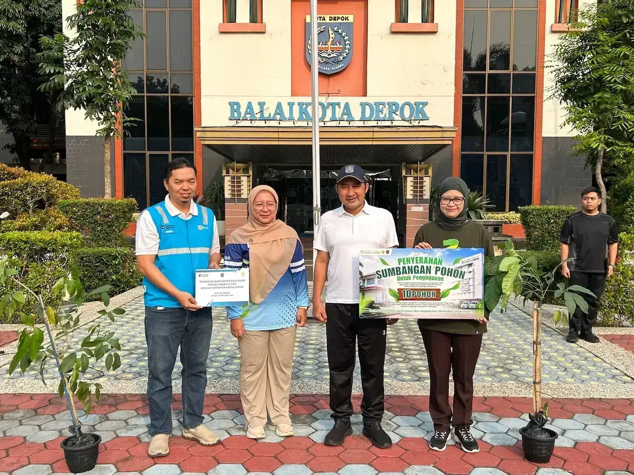Manager PLN UP3 Depok, Ramdani Agustiyansah dan Direktur Rumah Sakit Puri Cinere, Putri Nadia menyerahkan pohon secara simbolis kepada Wakil Wali Kota Depok, Chandra Rahmansyah pada apel pagi Aparatur Sipil Negara (ASN) di Lapangan Apel Balai Kota Depok, Jumat (09/10/26). (Sumber: Siaran Depok/AN Rafi)